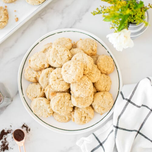 coconut vanilla bean mini cookies on a plate on a marble counter with fresh flowers.
