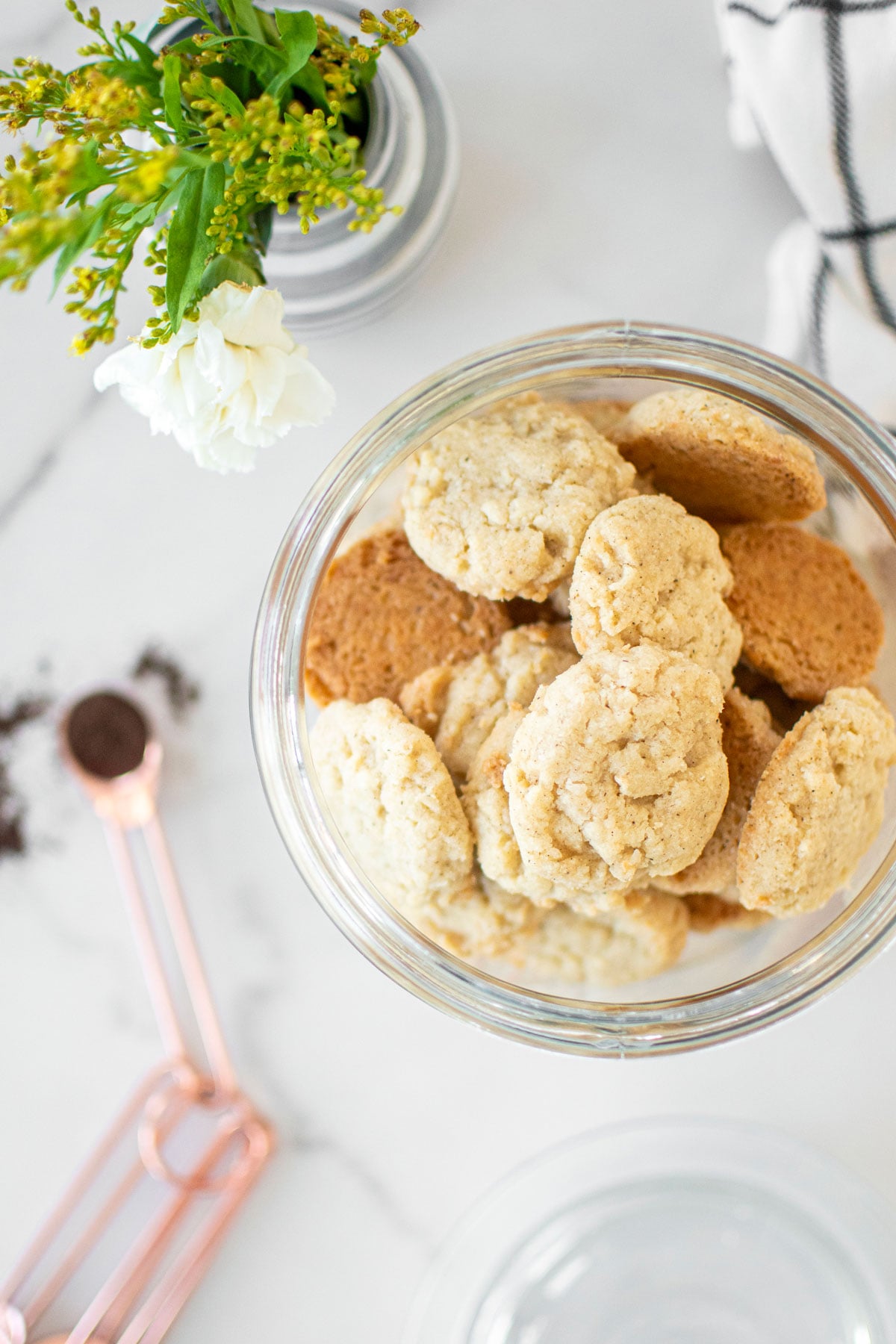 coconut vanilla bean mini cookies in a glass cookie jar on a marble counter.