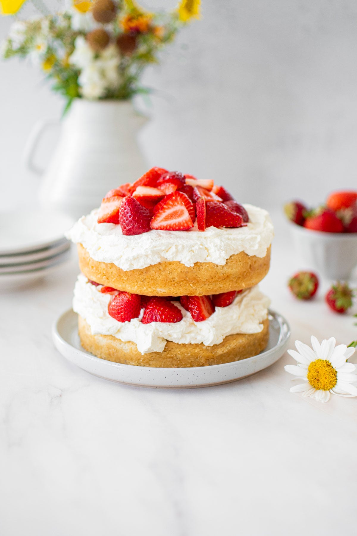 eggless strawberry shortcake on a marble countertop with cake plates and fresh strawberries.