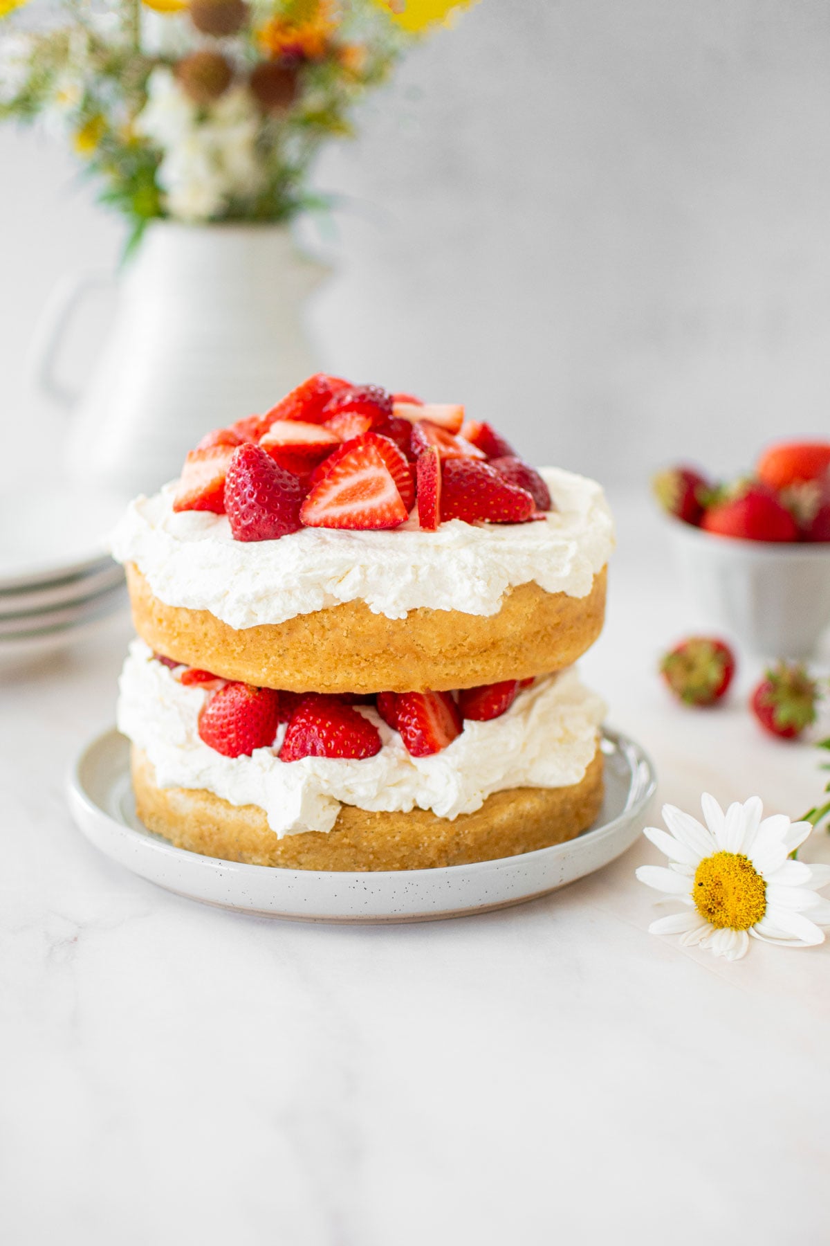 eggless strawberry shortcake on a marble countertop with cake plates and fresh strawberries.
