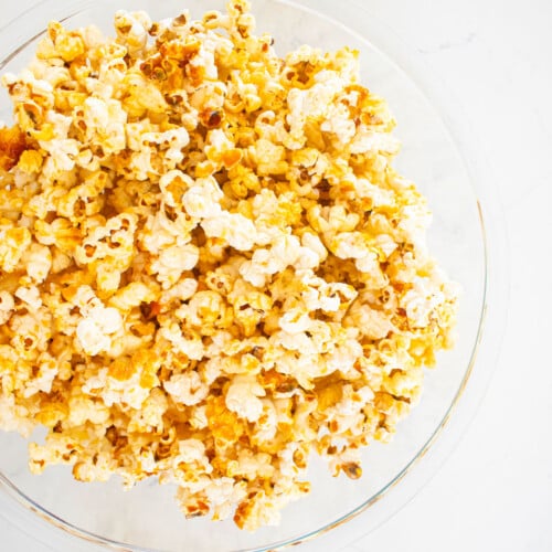 homemade kettle corn in a glass mixing bowl on a white marble countertop.