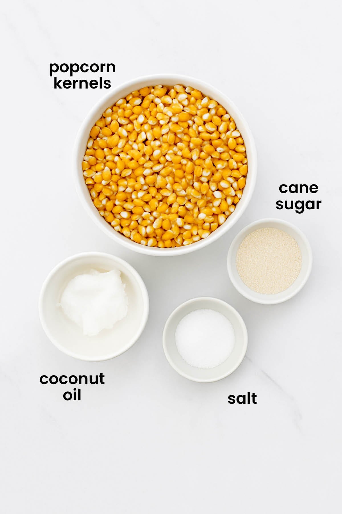 individual ingredients for homemade kettle corn with coconut oil laid out against a white background.