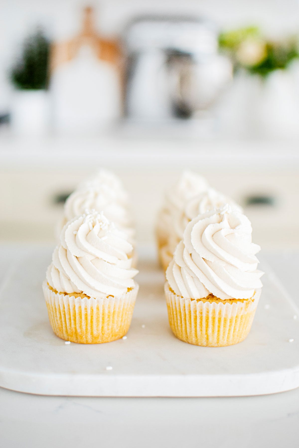 simple vanilla cupcakes on a marble serving board on a white marble counter.