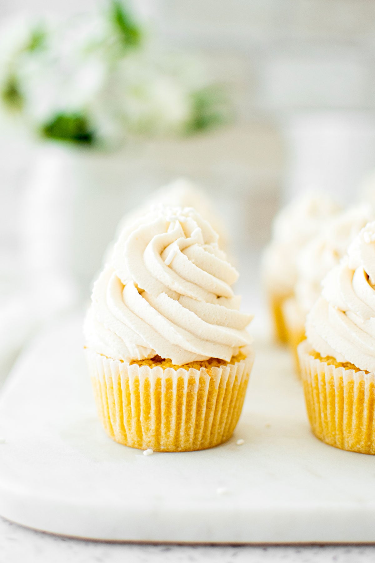 simple vanilla cupcakes on a marble serving board on a table with fresh flowers.