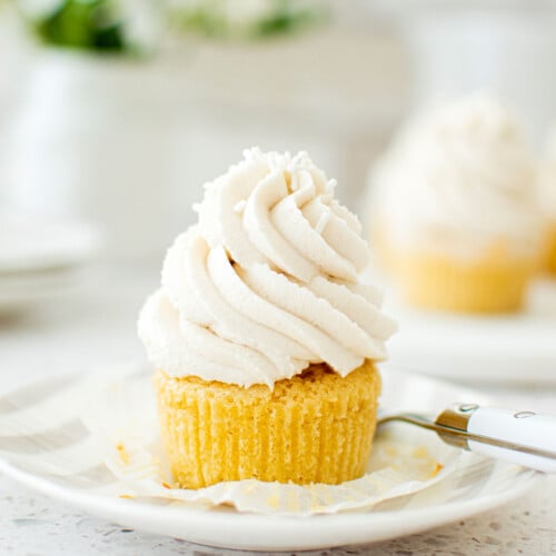 simple vanilla cupcake unwrapped on a stripe cake plate on a marble counter with fresh flowers.