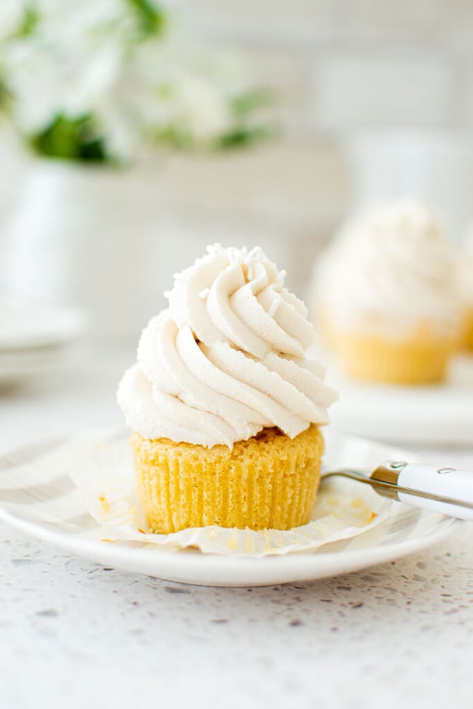 simple vanilla cupcake unwrapped on a stripe cake plate on a marble counter with fresh flowers.