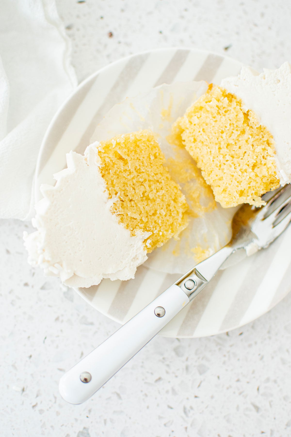 simple vanilla cupcake cut in half on a stripe cake plate on a marble counter.