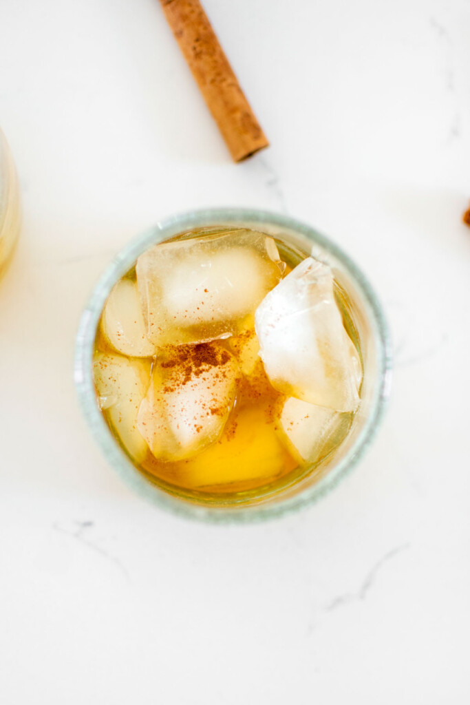 sparkling apple cider bourbon in a glass with ice on a white marble counter.