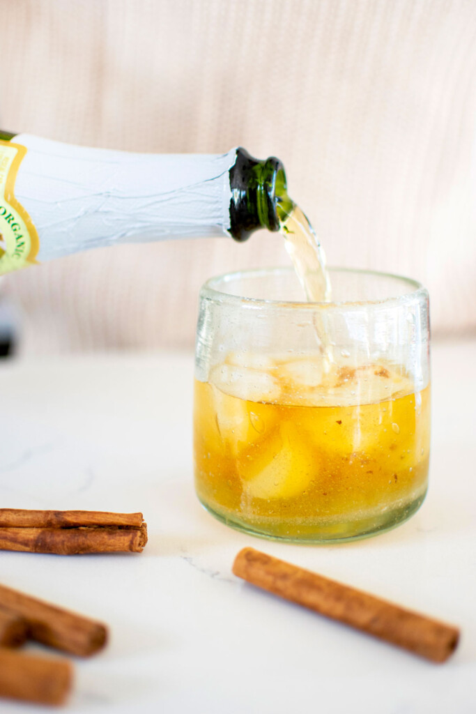 sparkling apple cider being poured into a bourbon and ice glass.