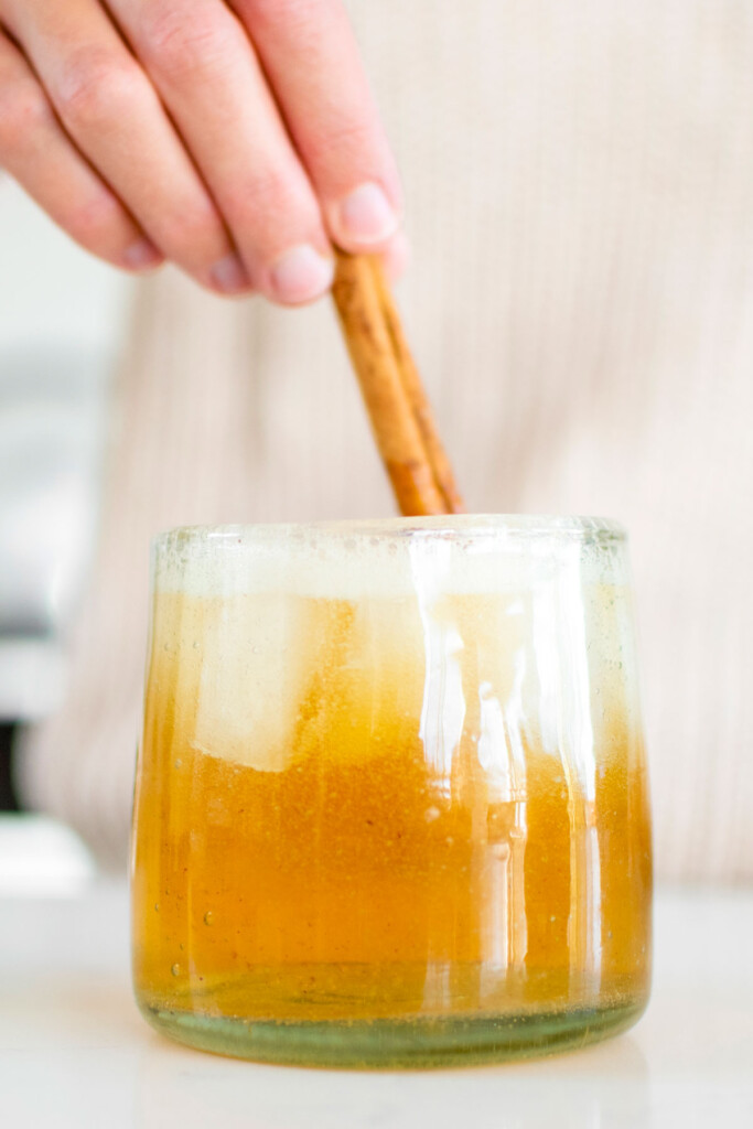 sparkling apple cider bourbon being stirred with a cinnamon stick.