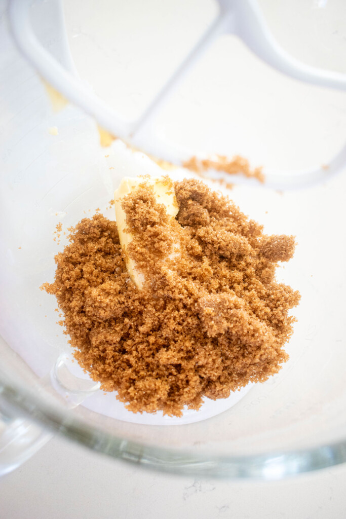 butter and brown sugar in a glass mixing bowl on a white marble counter.