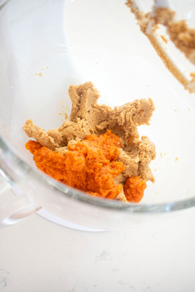 creamed butter and sugar with pumpkin puree in a glass mixing bowl on a white marble counter.