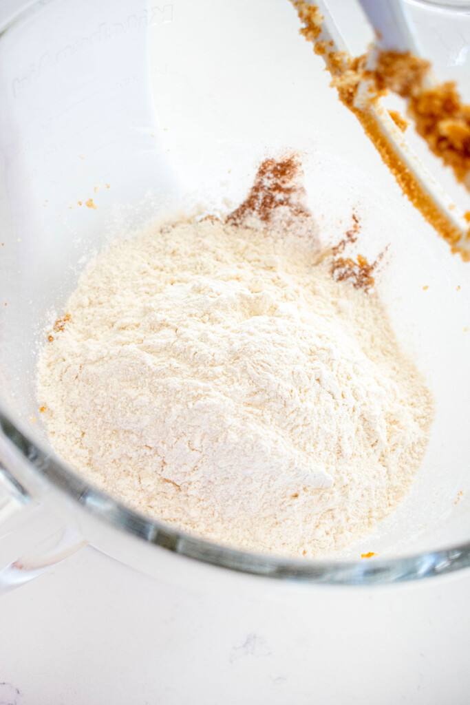 ingredients for pumpkin spice crinkle cookies in a glass mixing bowl on a white marble couter.