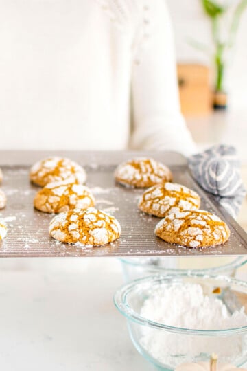 pumpkin spice crinkle cookies on a baking sheet being held by a woman.