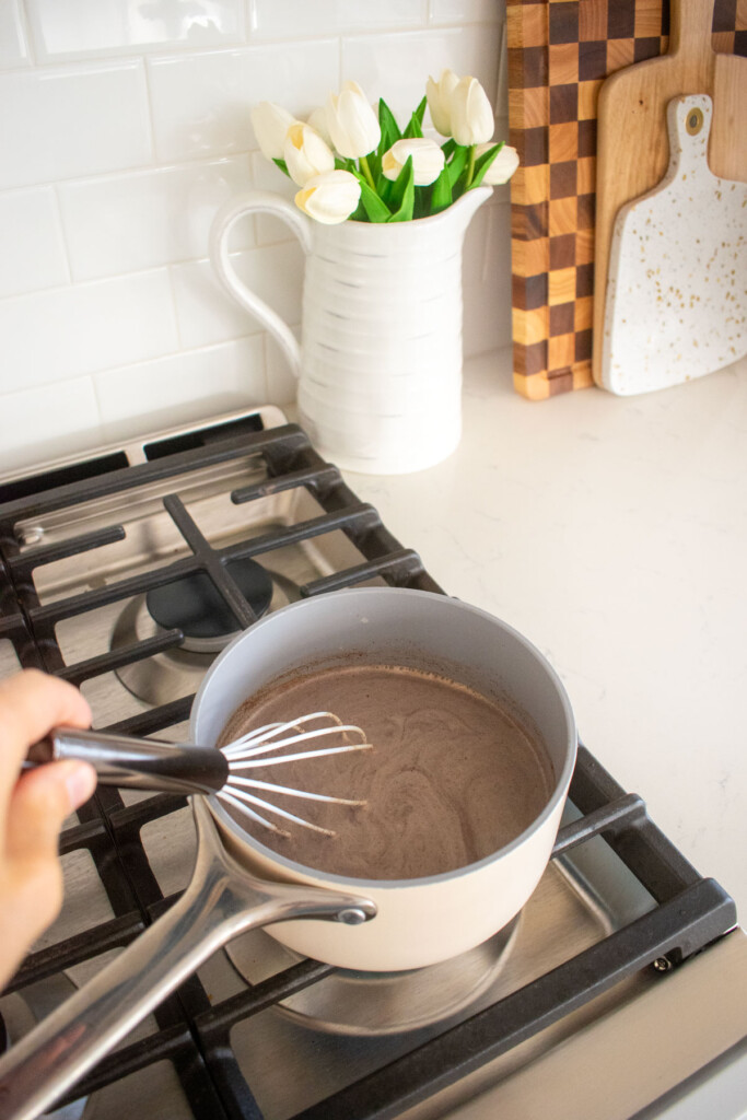 boozy pumpkin spice hot chocolate being whisked in a small pot on the stovetop.