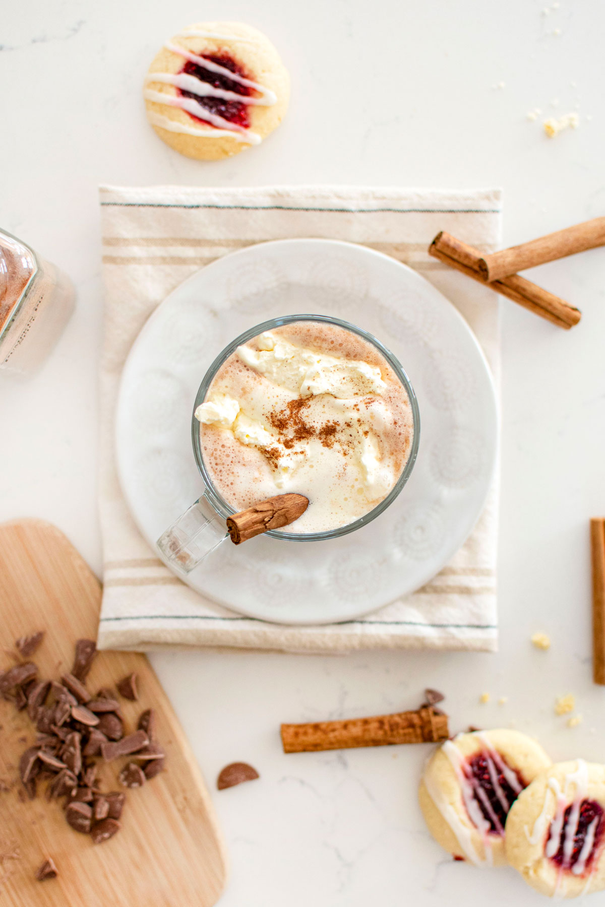 boozy pumpkin spice hot chocolate in a glass mug with whipped cream and a cinnamon stick on a plate on kitchen counter.