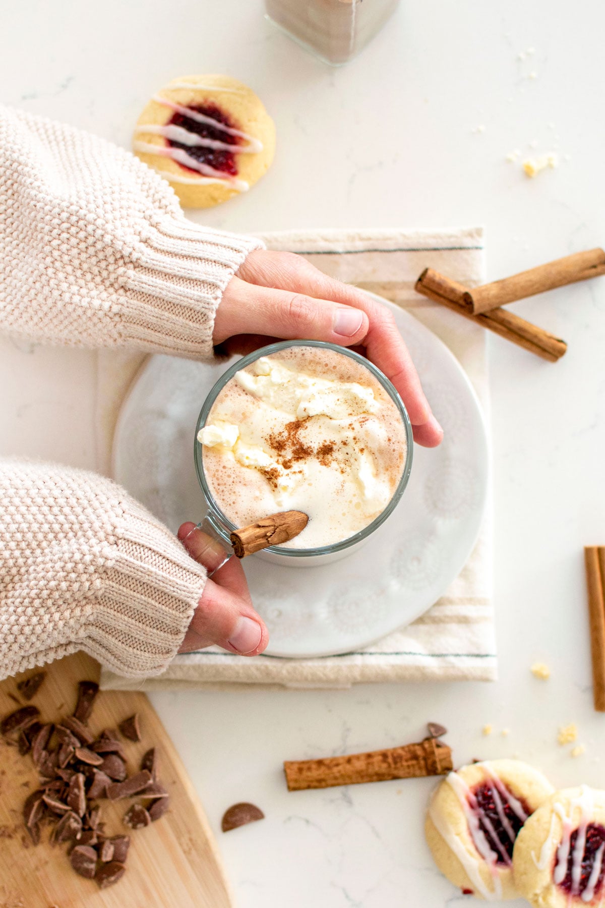 woman holding a glass mug with boozy pumpkin spice hot chocolate with whipped cream and a cinnamon stick.