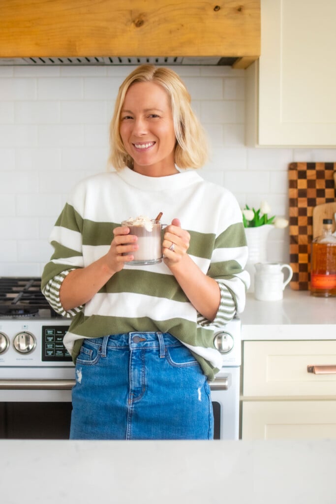 woman holding boozy pumpkin spice hot chocolate in the kitchen.