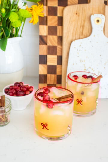 holiday punch with vodka in holiday drink glasses on a white marble counter with fresh cranberries and cinnamon sticks.