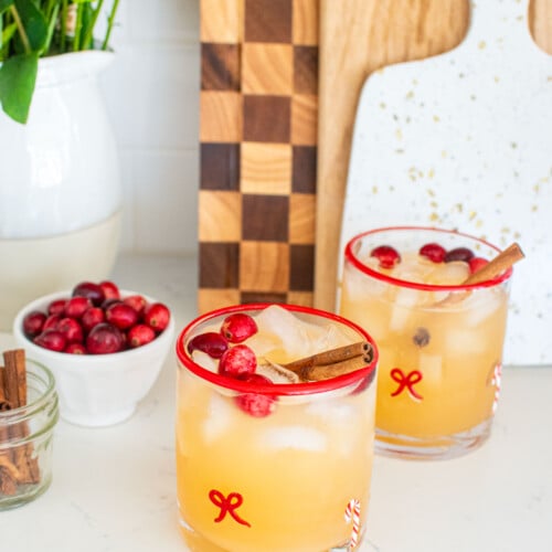 holiday punch with vodka in holiday drink glasses on a white marble counter with fresh cranberries and cinnamon sticks.