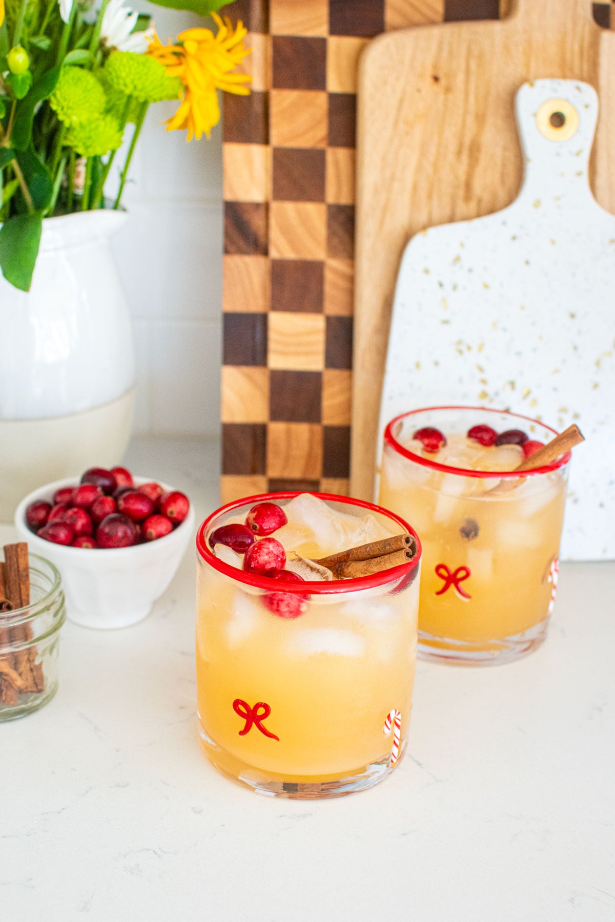 holiday punch with vodka in holiday drink glasses on a white marble counter with fresh cranberries and cinnamon sticks.