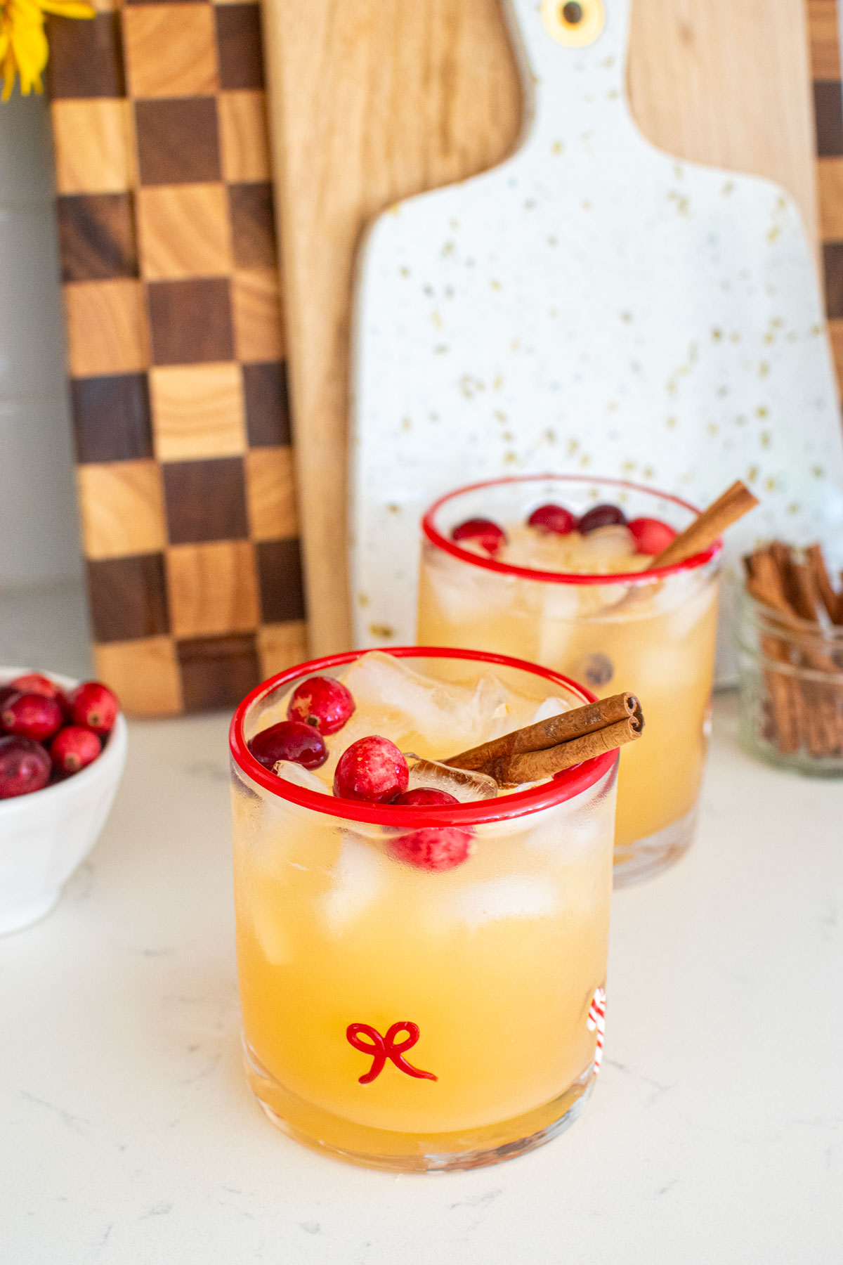 holiday punch with vodka in holiday drink glasses on a white marble counter with fresh cranberries and cinnamon sticks.