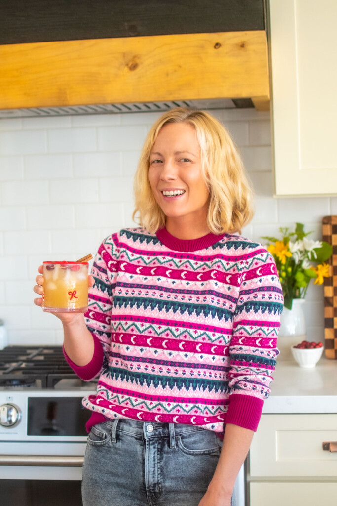 woman holding a holiday punch with vodka wearing a christmas sweater in the kitchen.