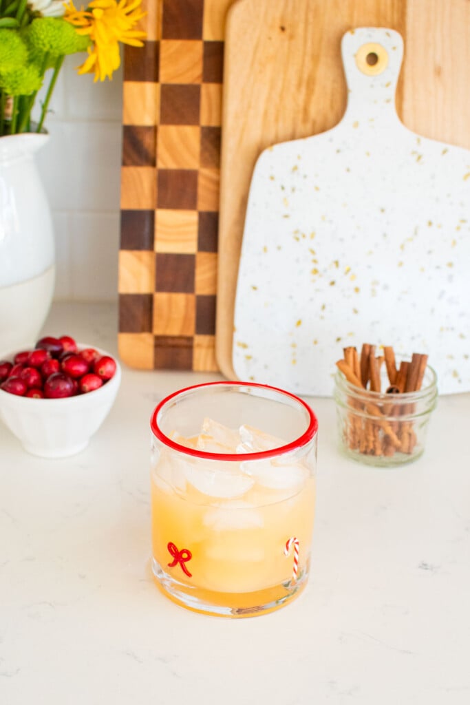 holiday punch with vodka being made in a holiday drink glass on a white marble counter with fresh cranberries and cinnamon sticks.