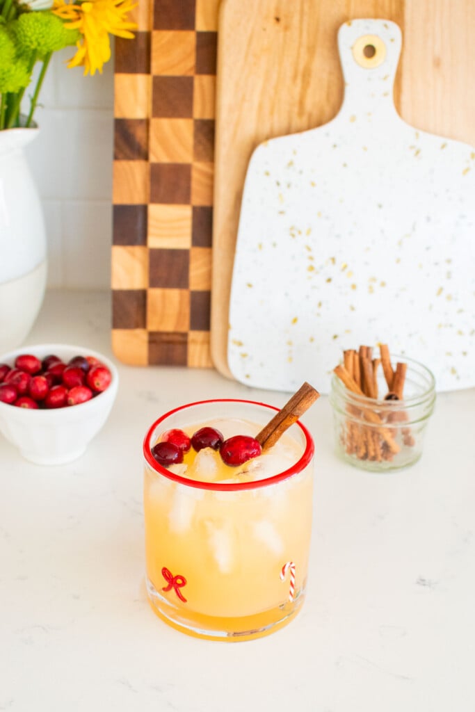 holiday punch with vodka being made in a holiday drink glass on a white marble counter with fresh cranberries and cinnamon sticks.
