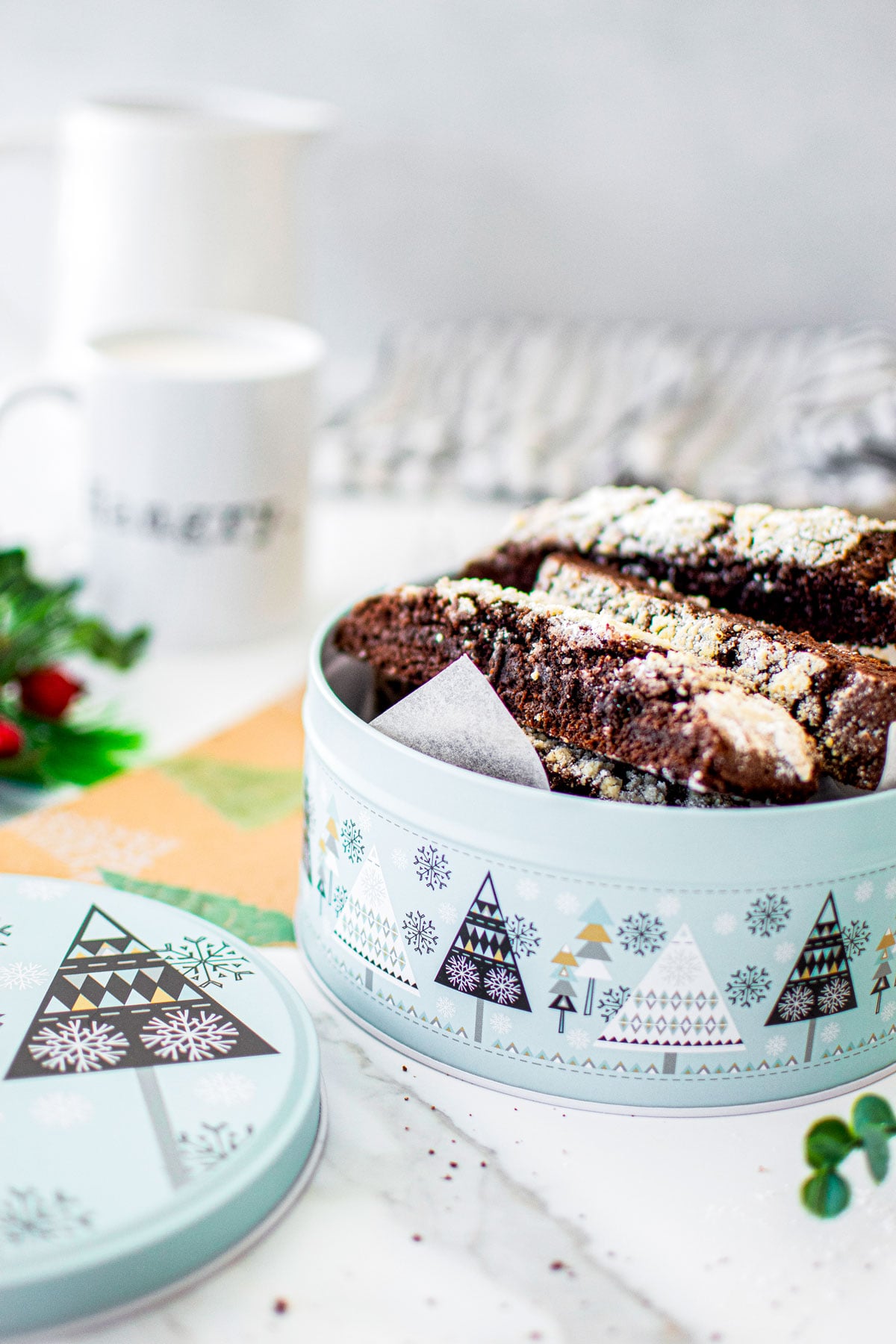 chocolate crinkle biscotti in a christmas tin on a white marble counter.