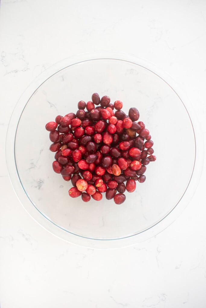 glass mixing bowl of cranberries on a white marble counter.