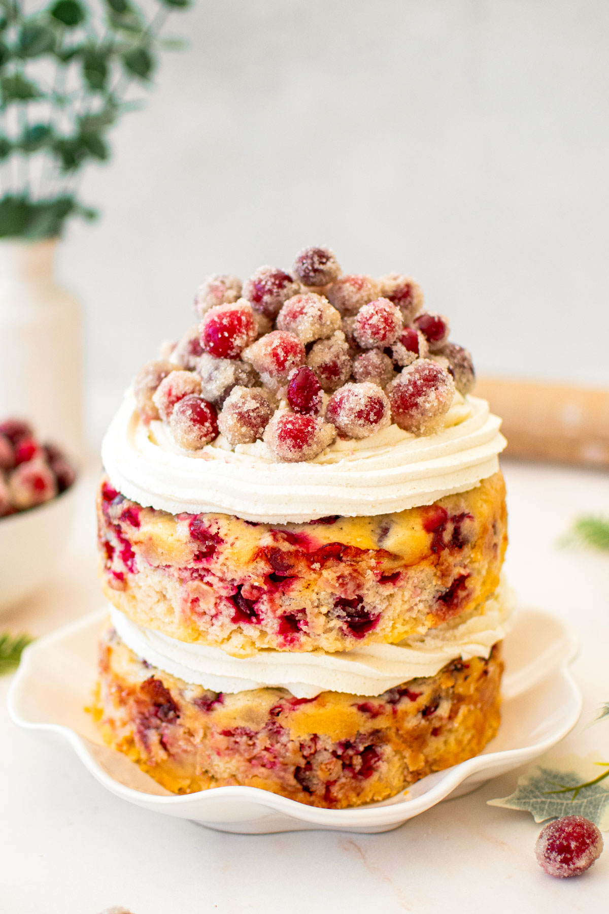 cranberry orange two layer naked cake with sugared cranberries on top on a marble counter.