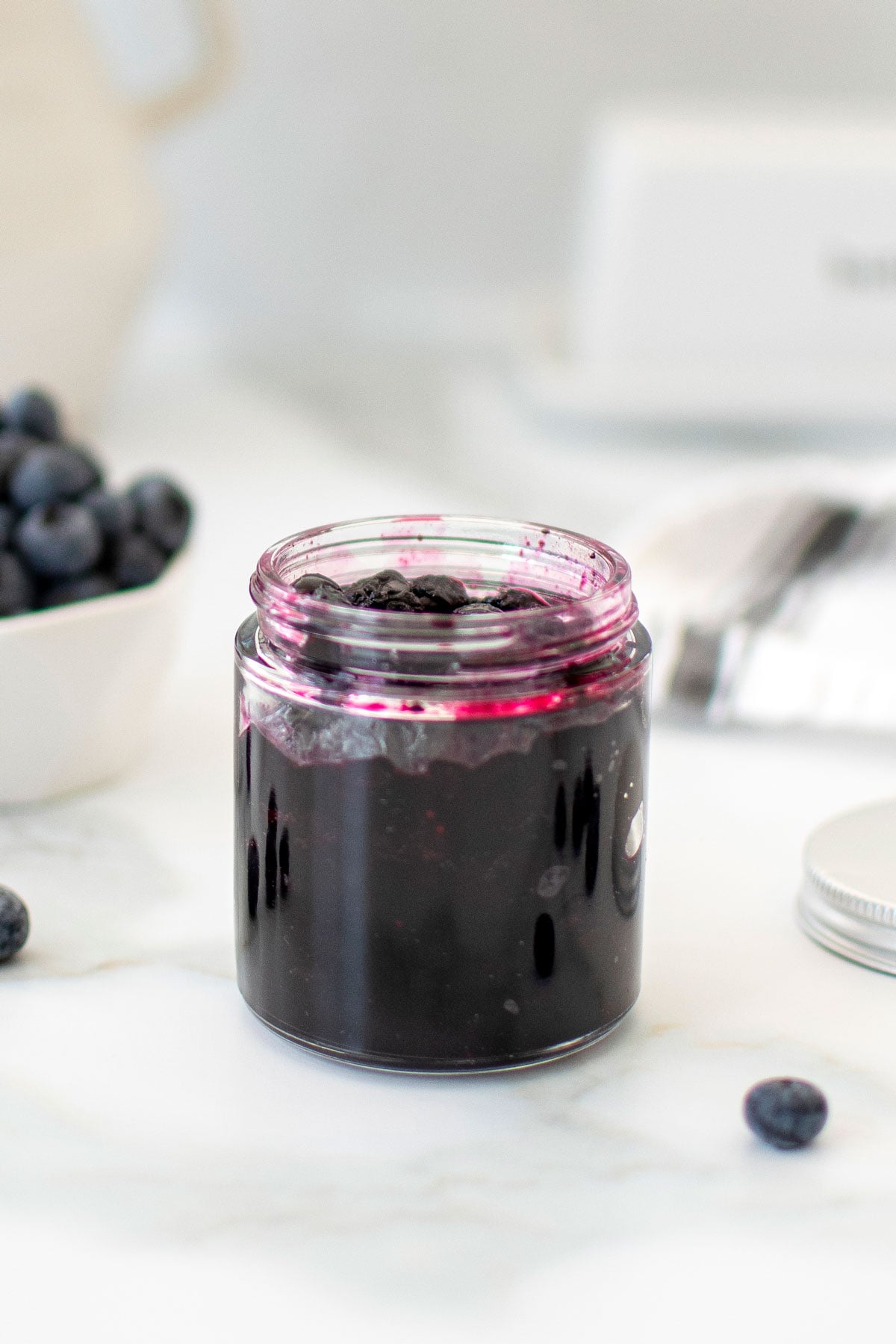glass jar of homemade blueberry preserves on a marble counter.