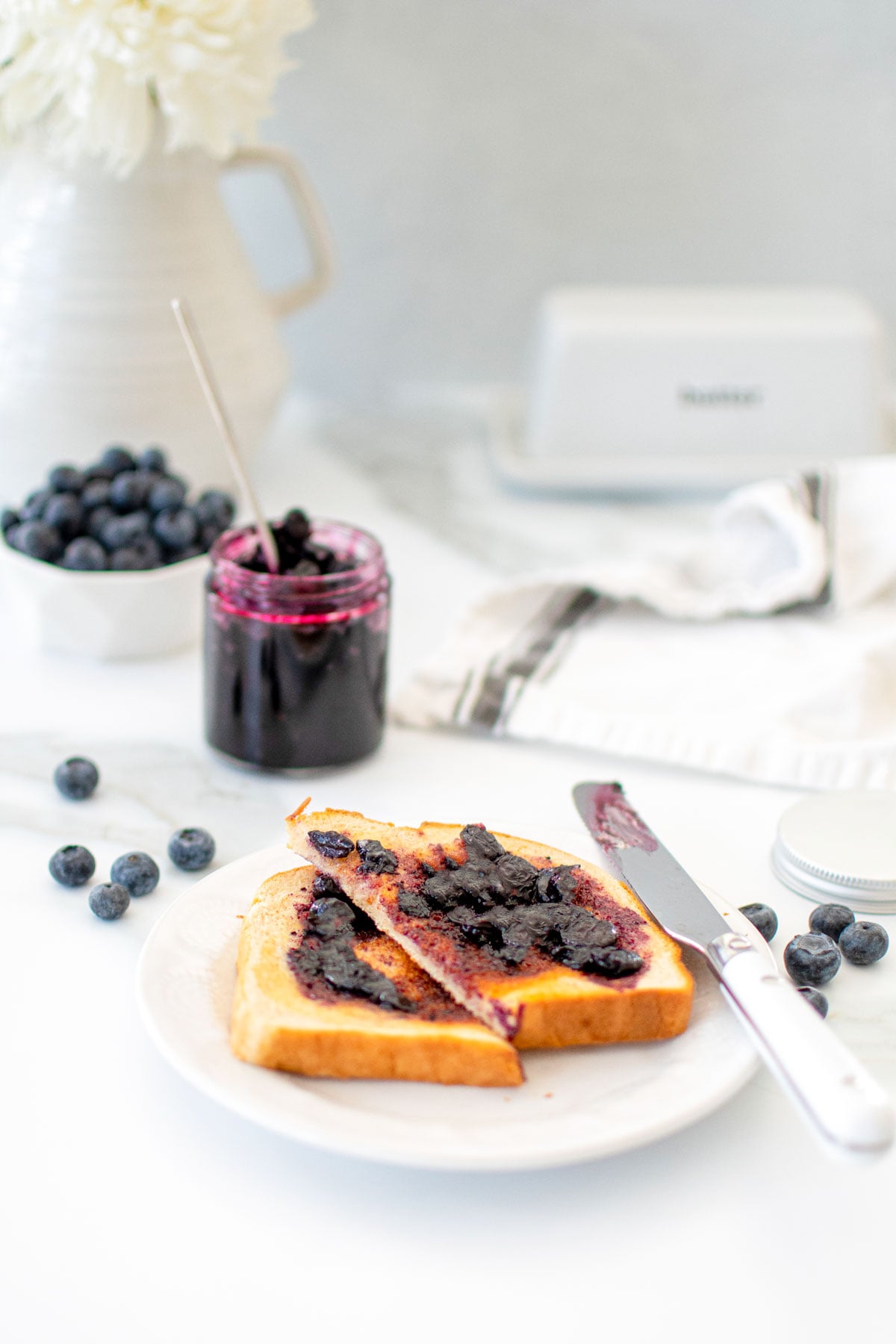 homemade blueberry preserves on sourdough toast cut in half on a white plate on a marble counter.