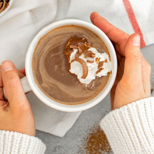 woman holding a mug of dark hot chocolate with homemade whipped cream on top.