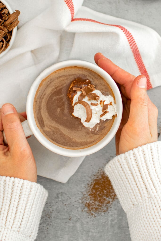 woman holding a mug of dark hot chocolate with homemade whipped cream on top.