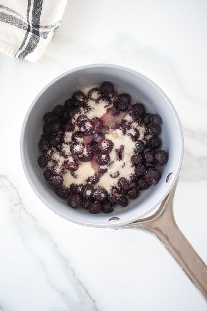 small pot with blueberries, cane sugar and lemon juice on a marble counter.