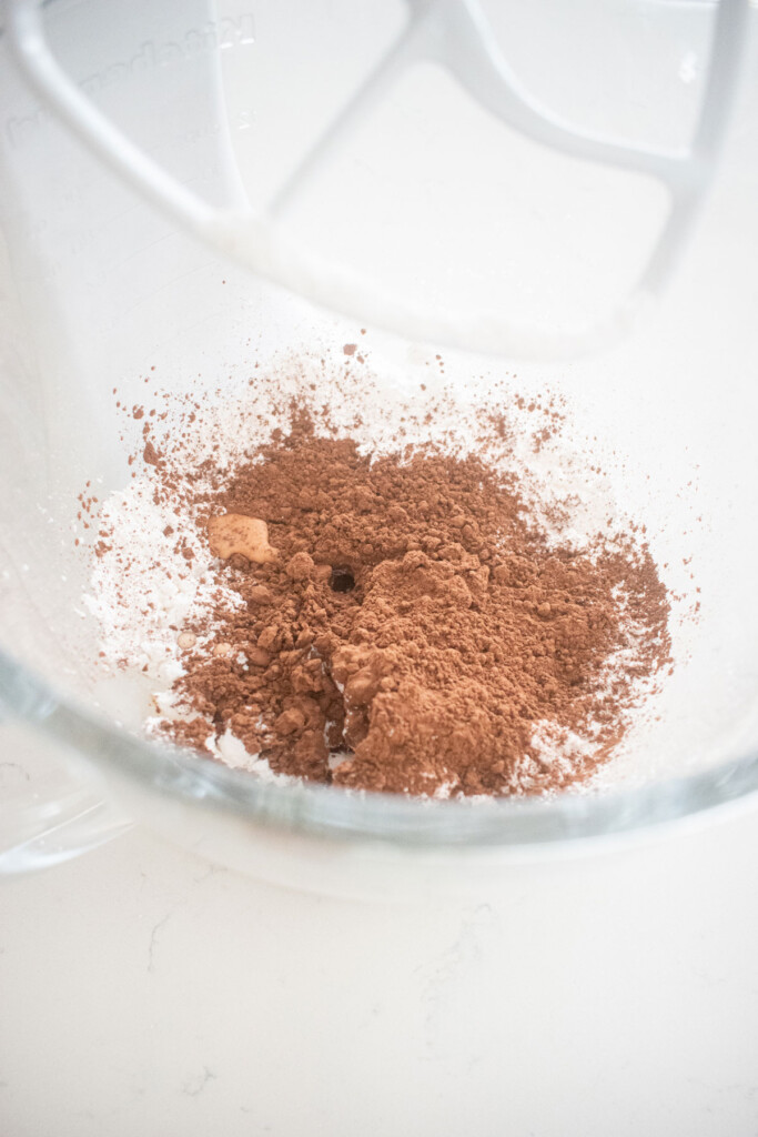 ingredients for hot chocolate bombs without a mold in a glass mixing bowl on a white marble counter.