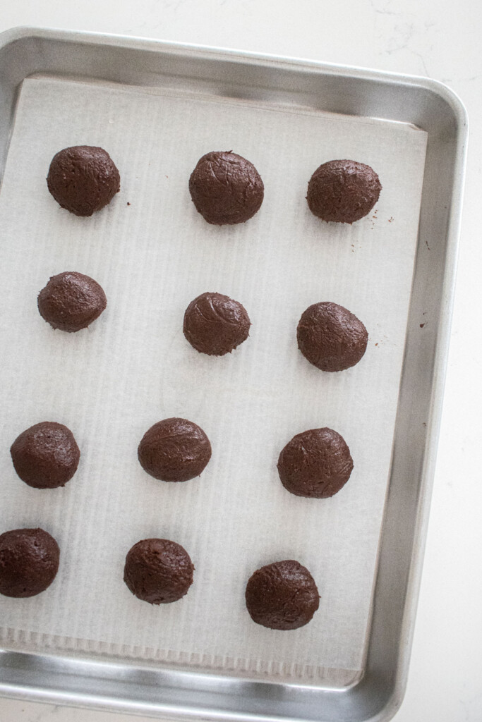 hot chocolate bombs rolled into balls on a baking sheet on white marble counter.