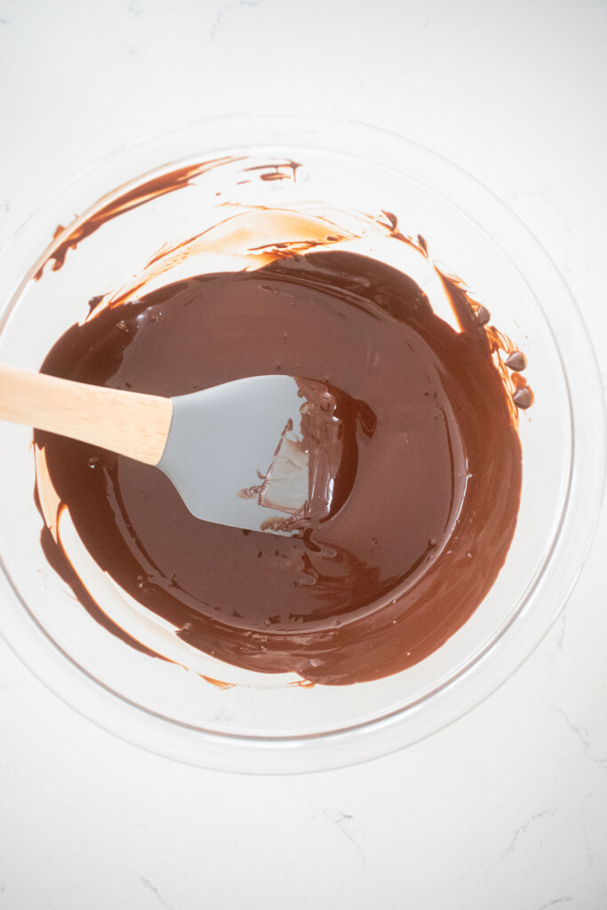 melted chocolate in a glass mixing bowl on a white marble countertop.