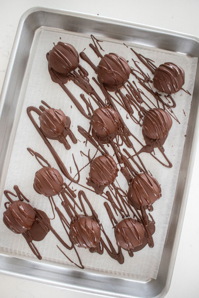 hot chocolate bombs being drizzled with chocolate on a sheet pan.