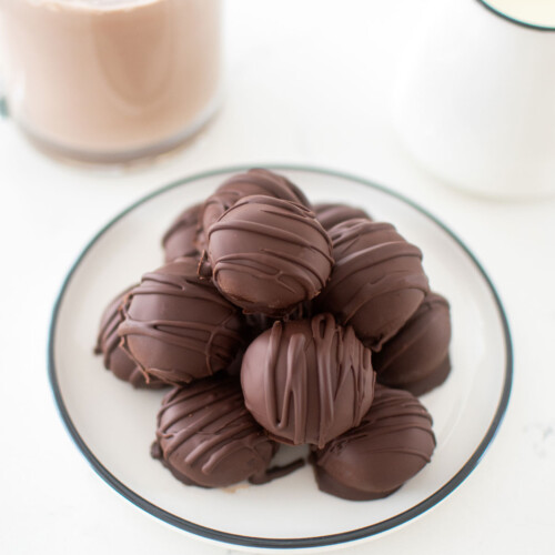 plate of hot chocolate bombs on the kitchen counter with a mug of milk and hot cocoa.