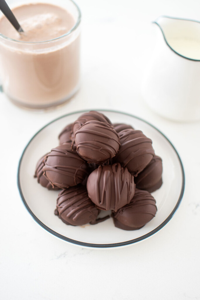 plate of hot chocolate bombs on the kitchen counter with a mug of milk and hot cocoa.