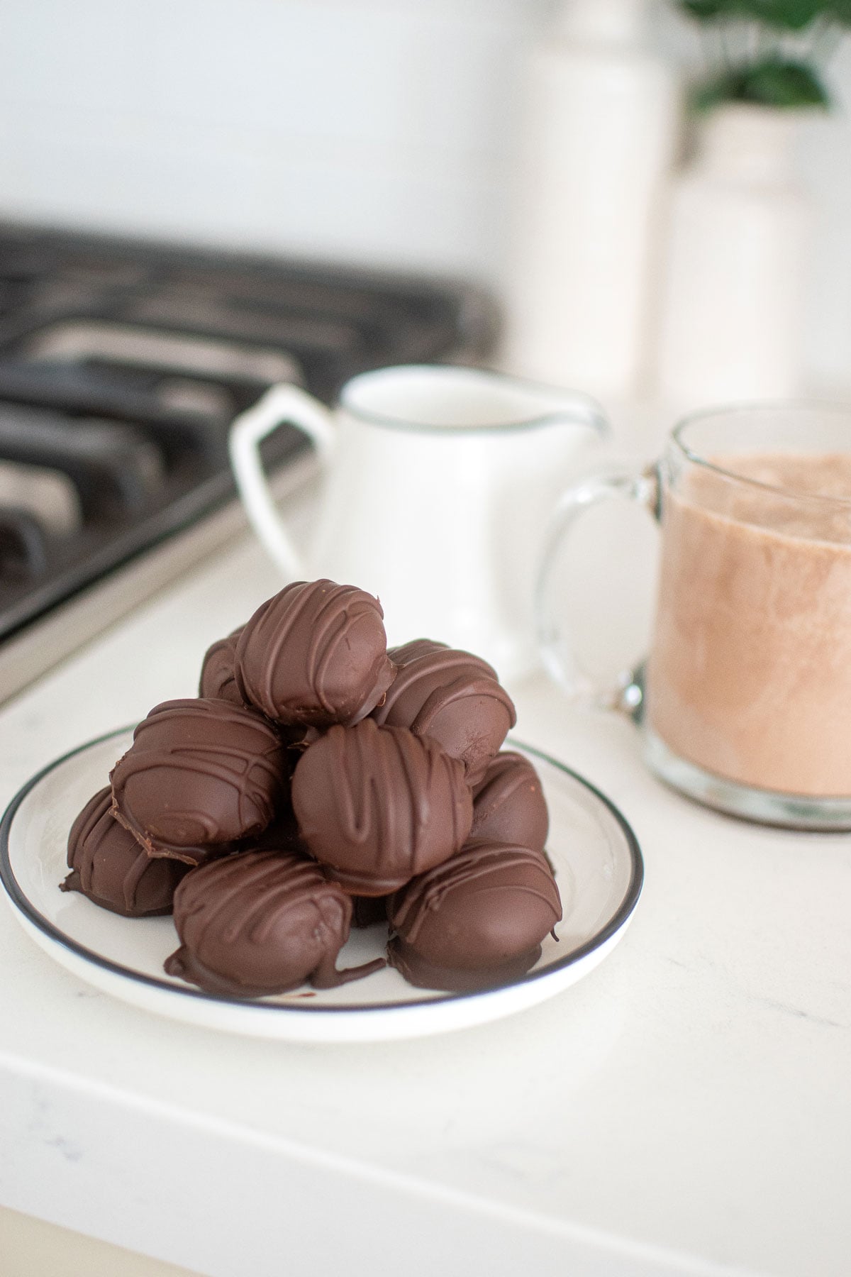 plate of hot chocolate bombs on the kitchen counter with a hot chocolate and mug of milk.