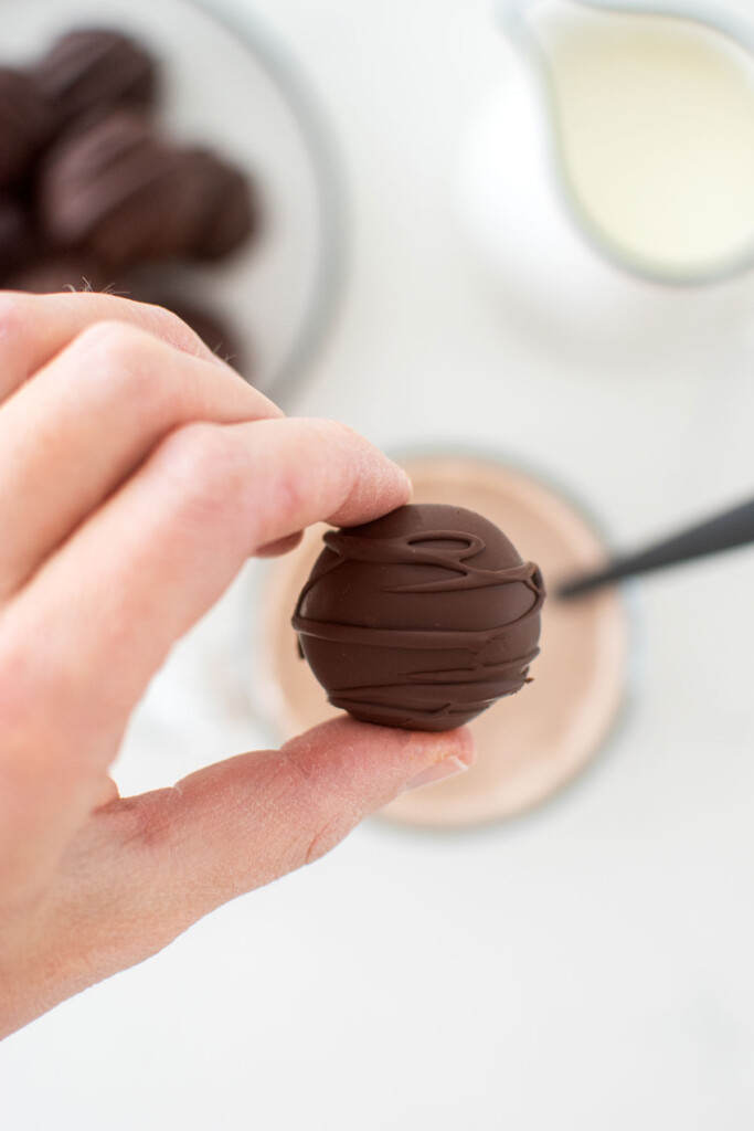 woman holding a hot chocolate bomb over the a mug of hot chocolate.