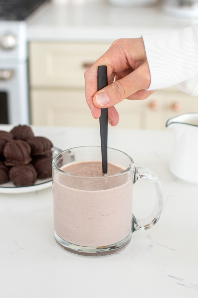 hot chocolate bomb being stirred into a cocoa in a glass much at the kitchen counter.