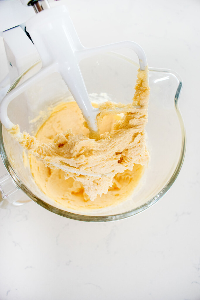 creamed butter sugar and vanilla in a glass stand mixing bowl on a white marble counter.
