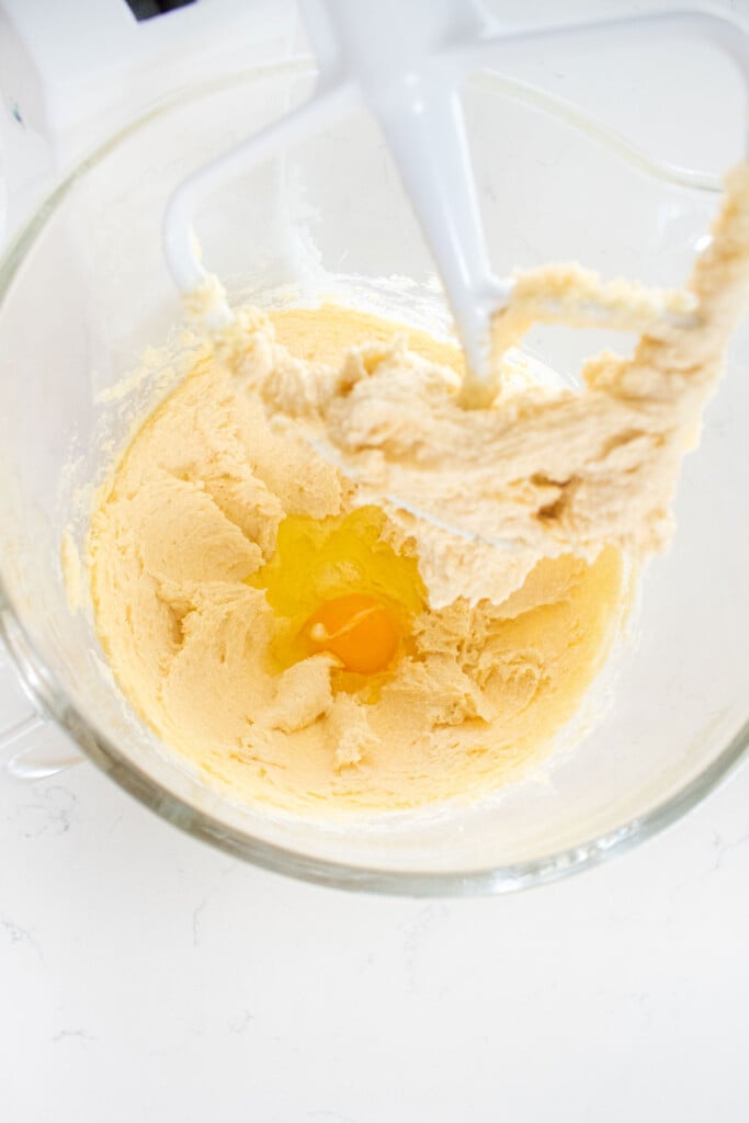 creamed butter sugar and vanilla with an egg in a glass stand mixing bowl on a white marble counter.