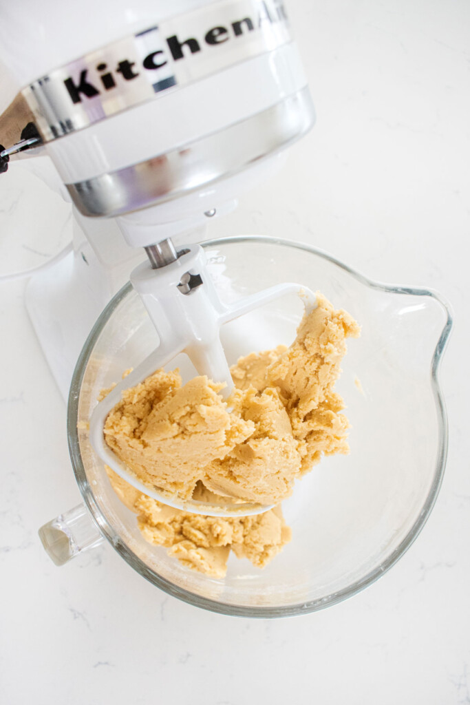 shortbread cookie dough in a glass stand mixing bowl on a white marble counter.