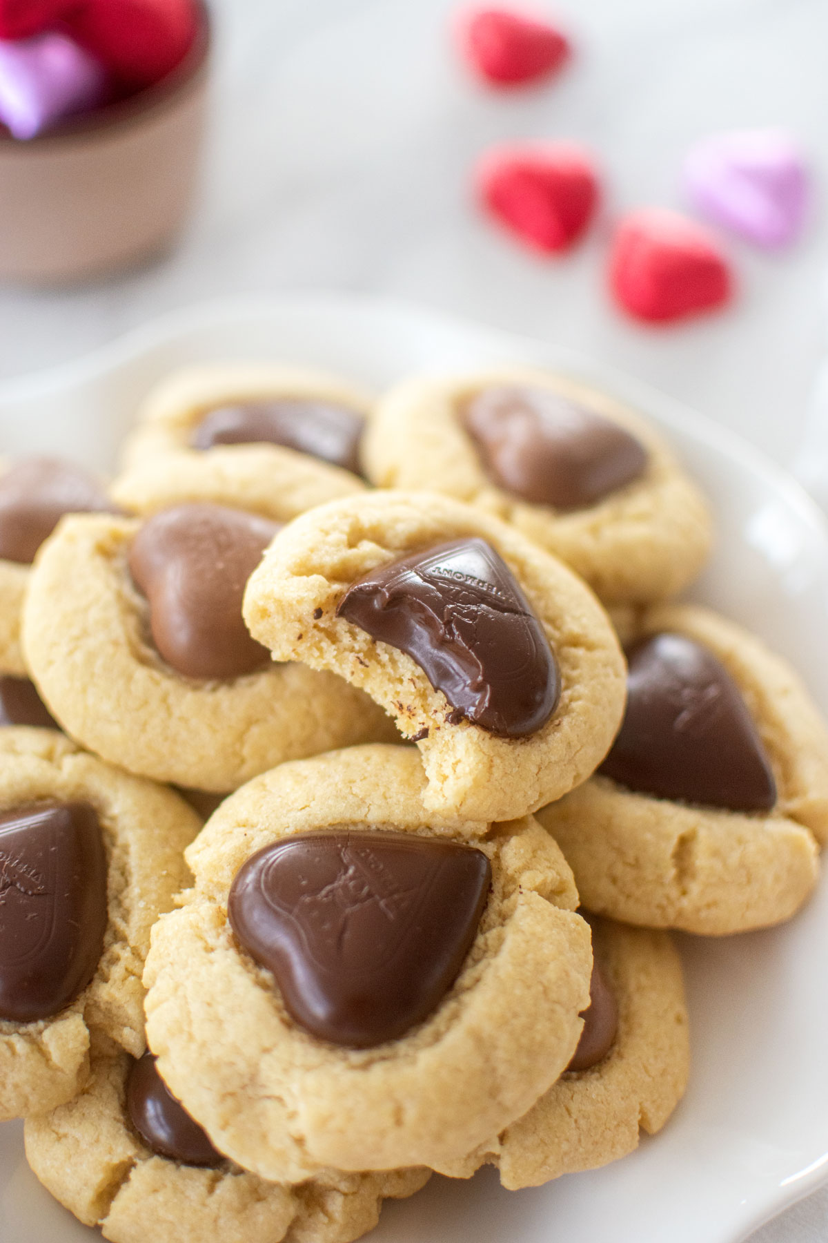 chocolate heart thumbprint cookies on a plate, one with a bite taken out on a white marble counter.